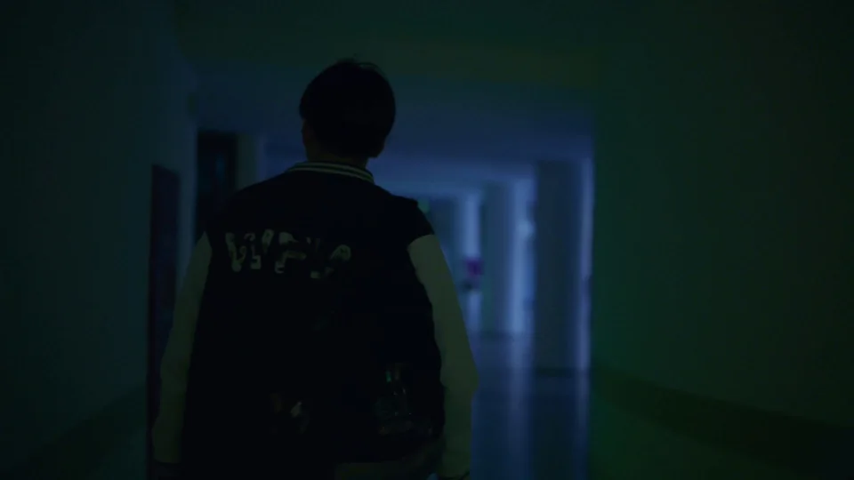 A student walking through a blue-lit corridor in the short film 復